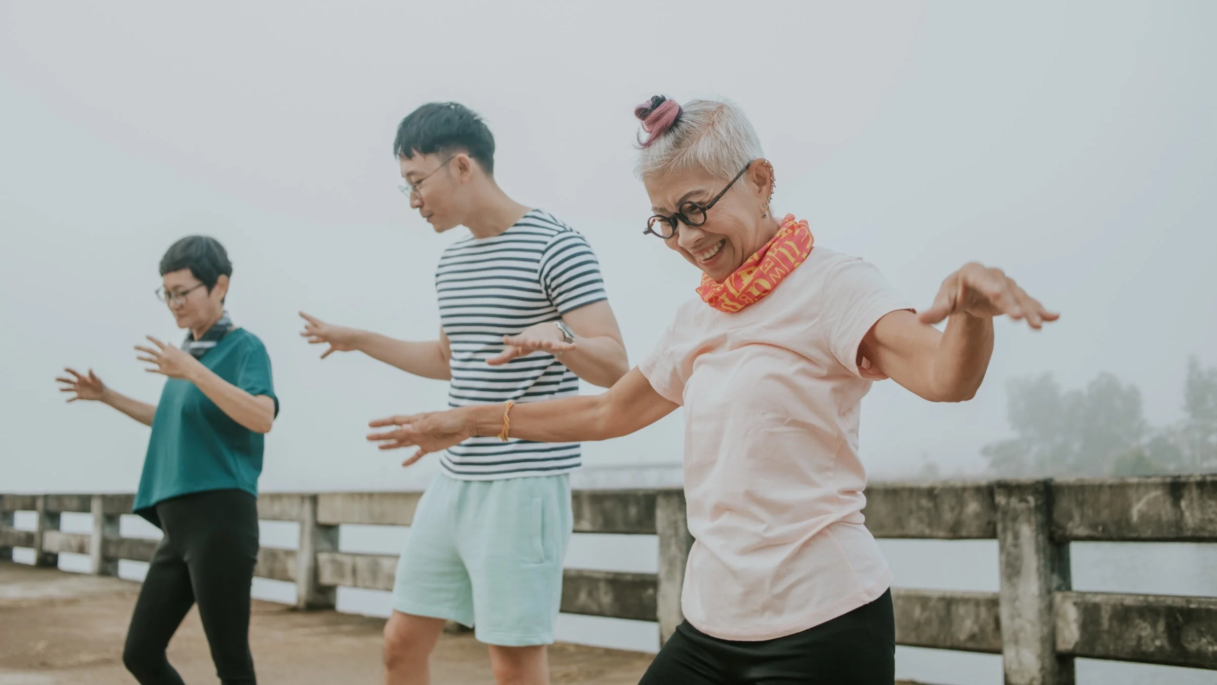 Older senior woman working out and stretching with others outside on a pier.