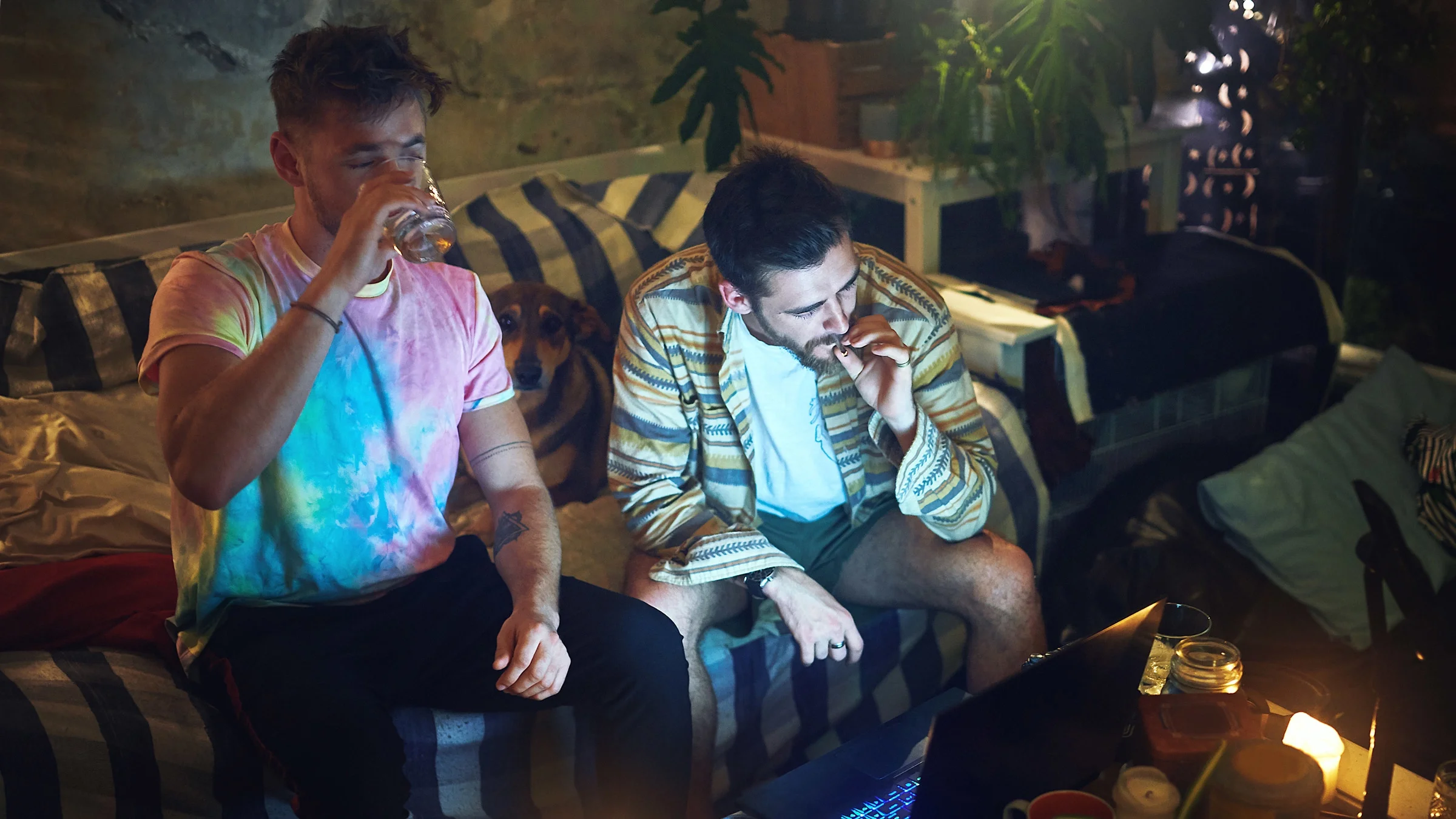 Two friends smoking weed and drinking on a couch.