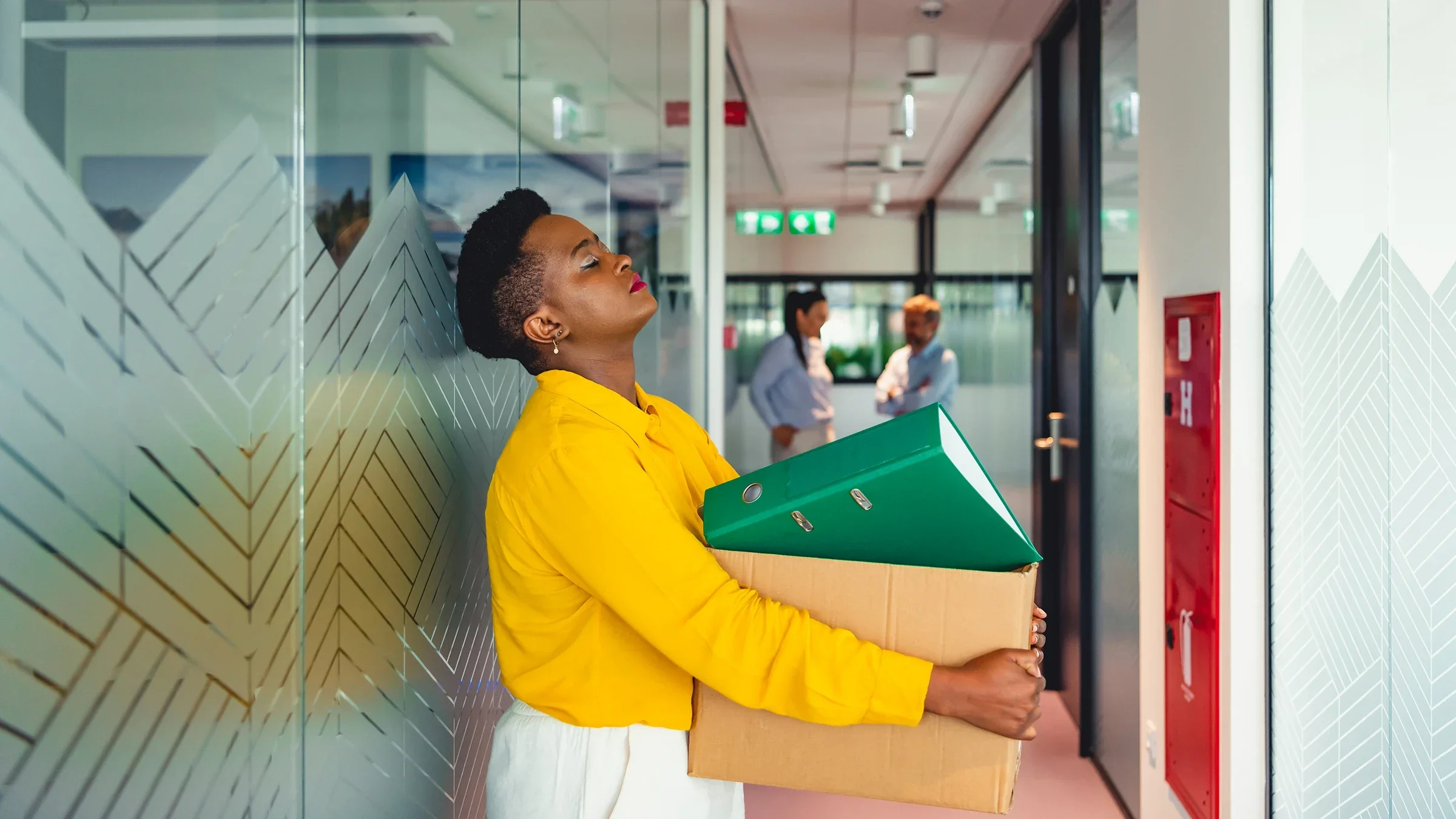 Exhausted woman leaning against the office hallway wall with her box of desk items after quitting.
RealPeopleGroup/E+ via Getty Images