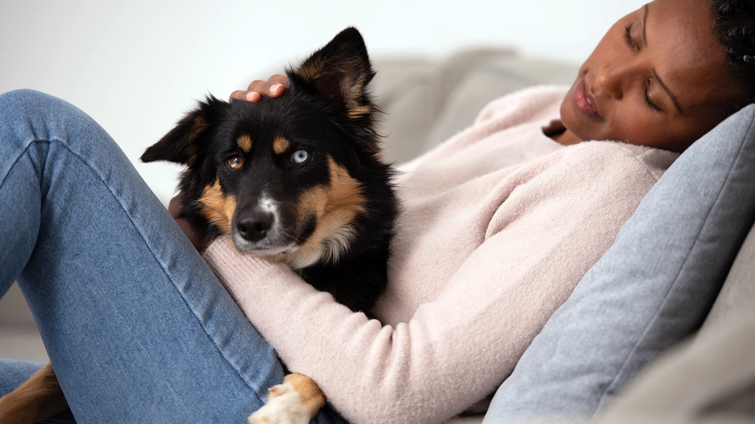 A woman is petting her dog while laying on the sofa.
