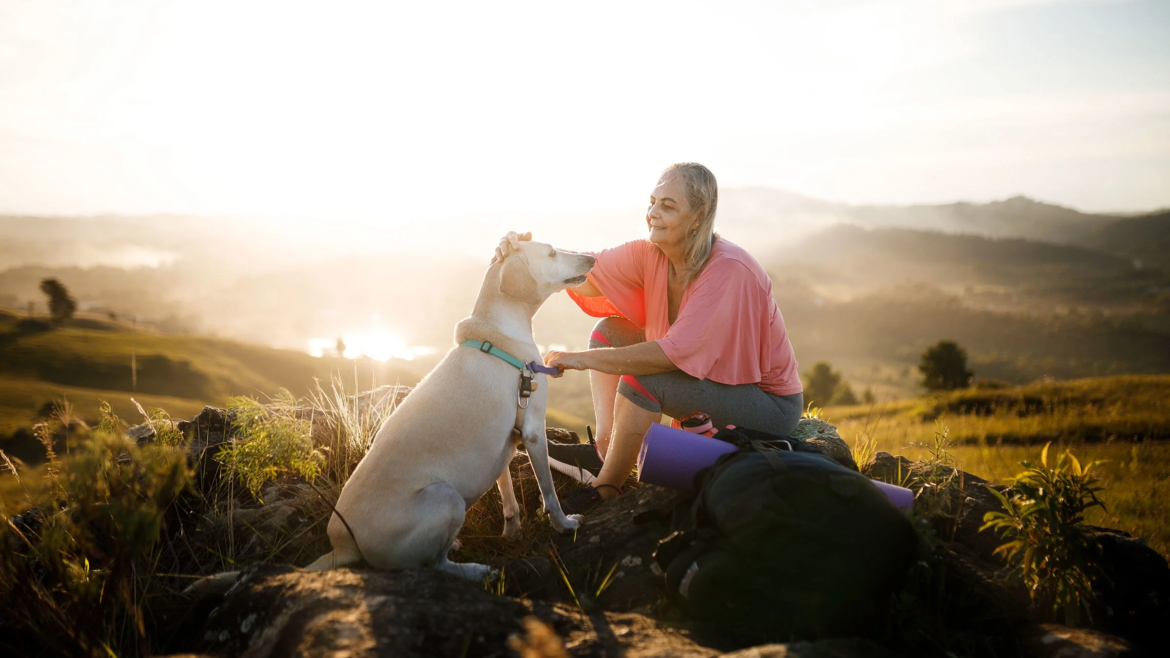 A woman sits on rocks and pets her dog.