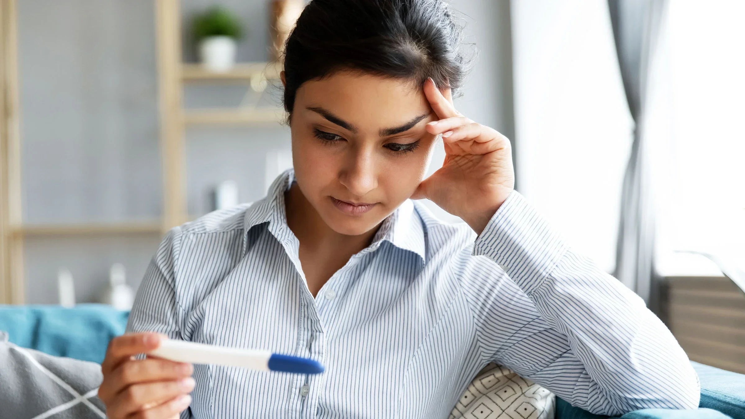 A woman holds and looks at a pregnancy test, waiting for the results. 
fizkes/iStock via Getty Images Plus    