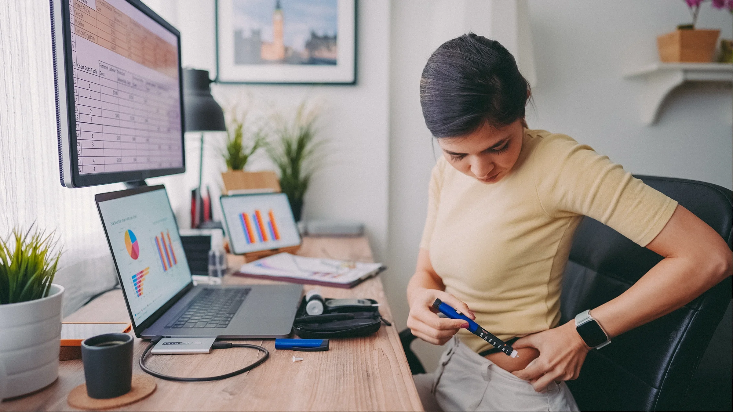 Woman sitting at her at-home desk using an insulin pen on her abdomen.