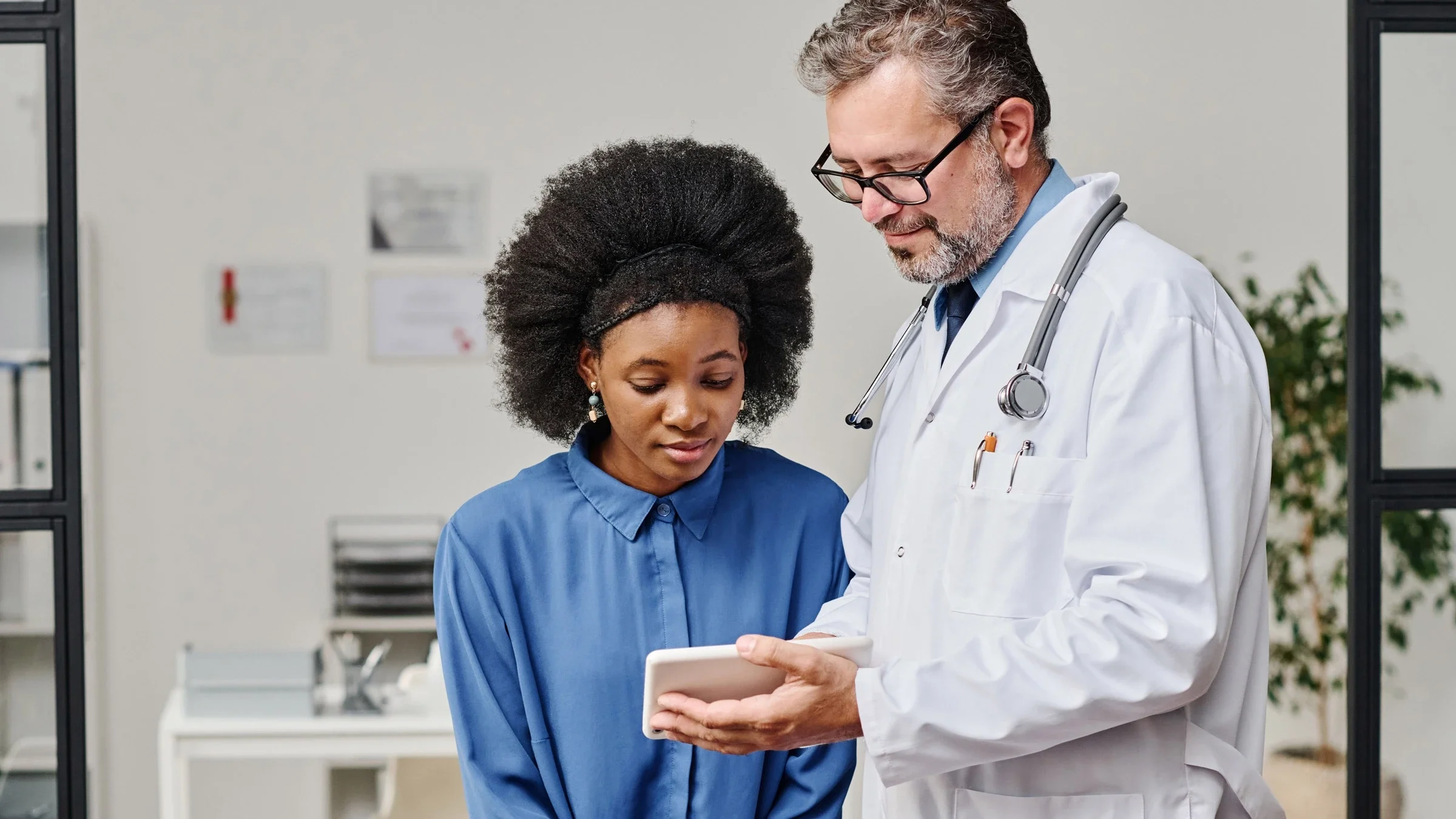 A doctor showing a tablet to a Black female patient.