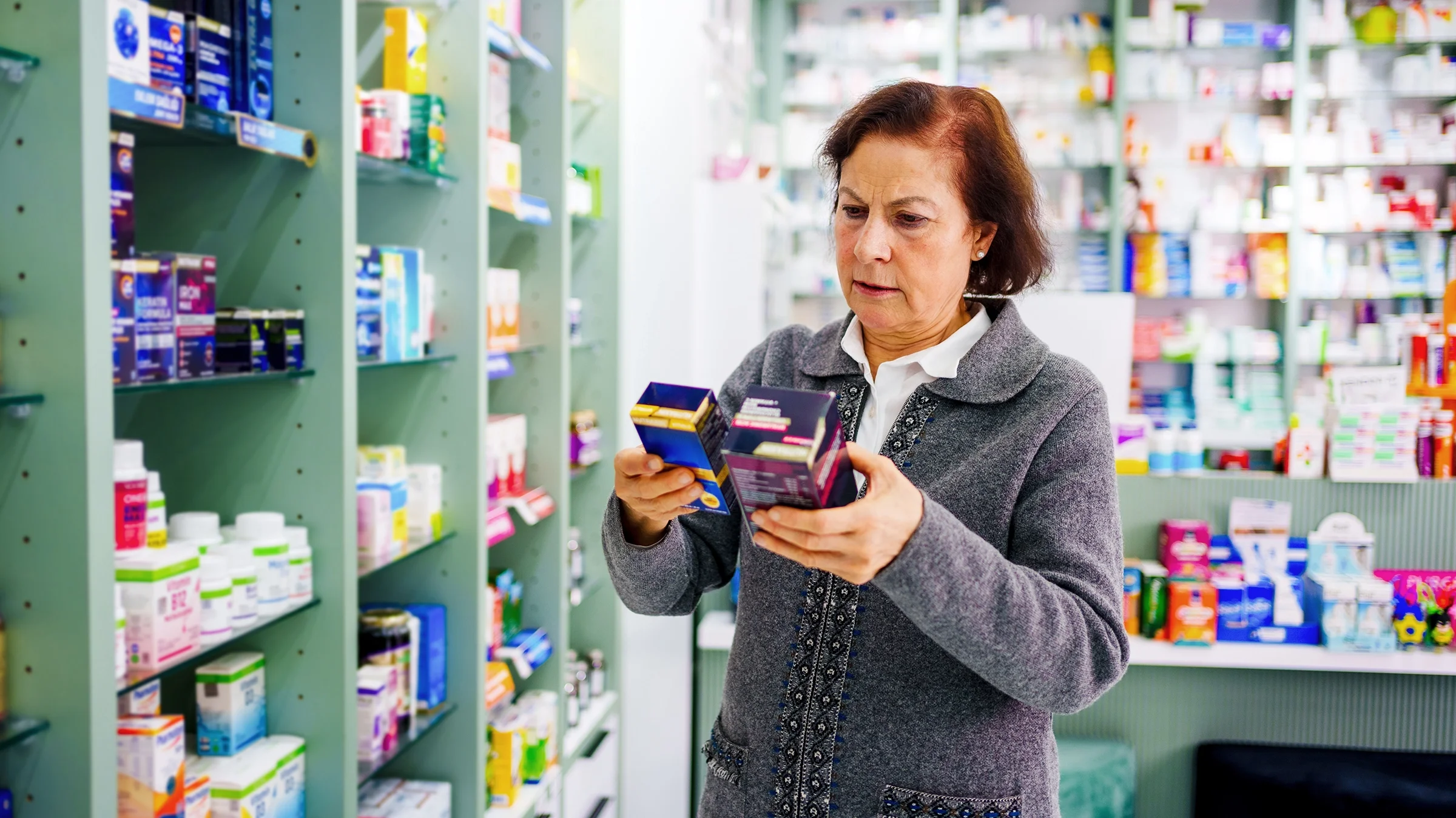 A woman reads the back of supplements boxes at the pharmacy. 