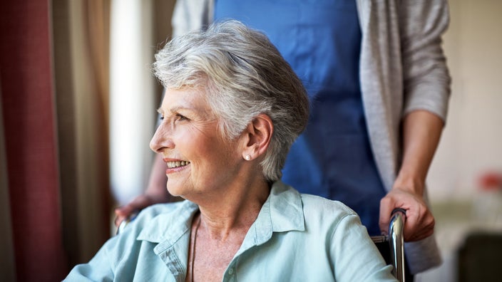 An older woman smiles while sitting in a wheelchair.