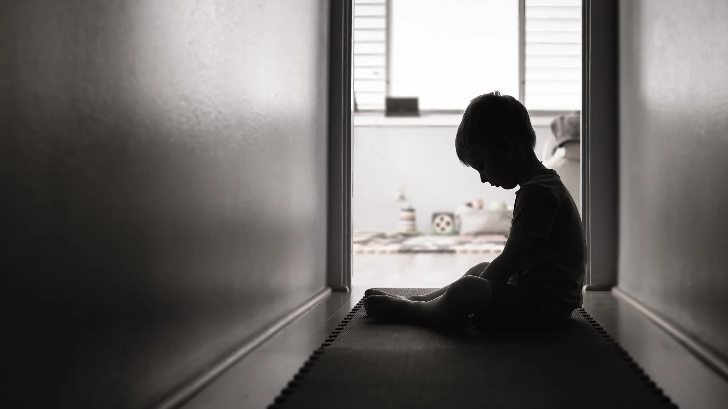 A boy who is sitting alone in a hallway is seen in silhouette.