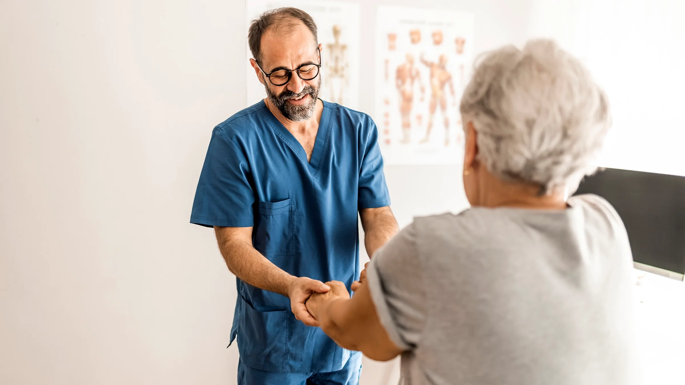 Older male nurse helping a patient in the exam room.