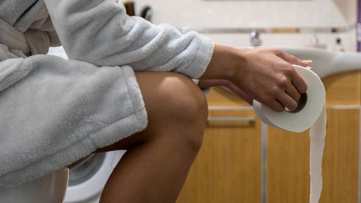 A cropped shot of someone sitting on a toilet, holding a toilet paper roll. 