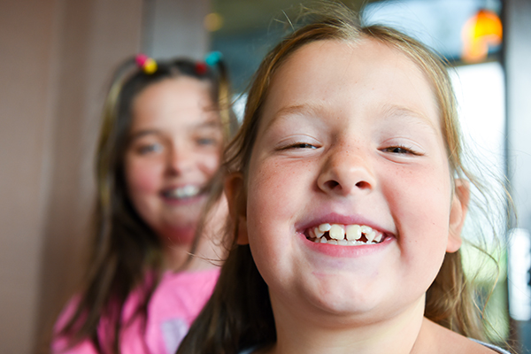 Close-up of two cute smiling little girls with chubby cheeks, one is in focus and the other is in the background out of focus.