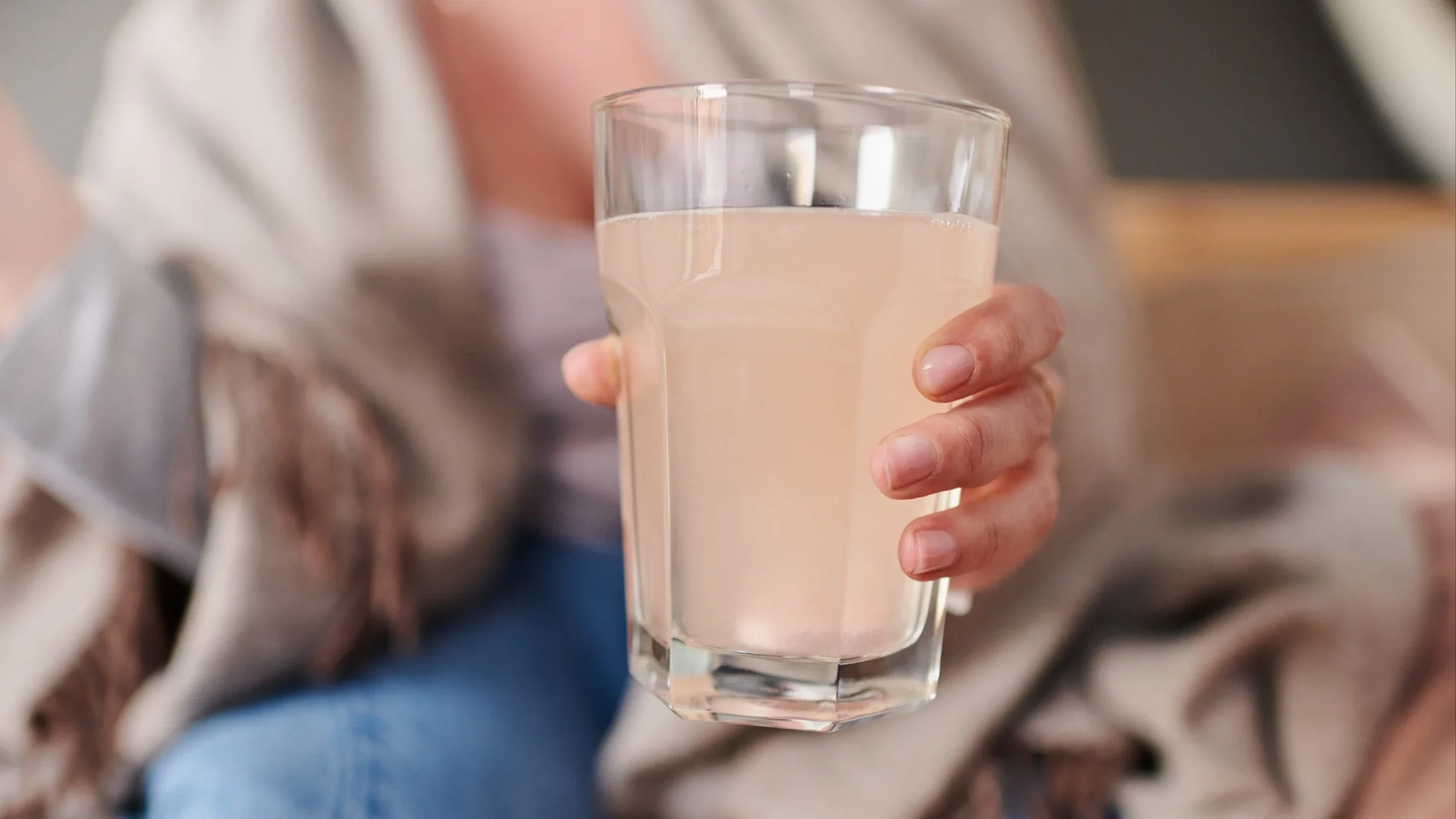 Close-up of a woman holding out a glass of water that has dissolved vitamin C powder in it.