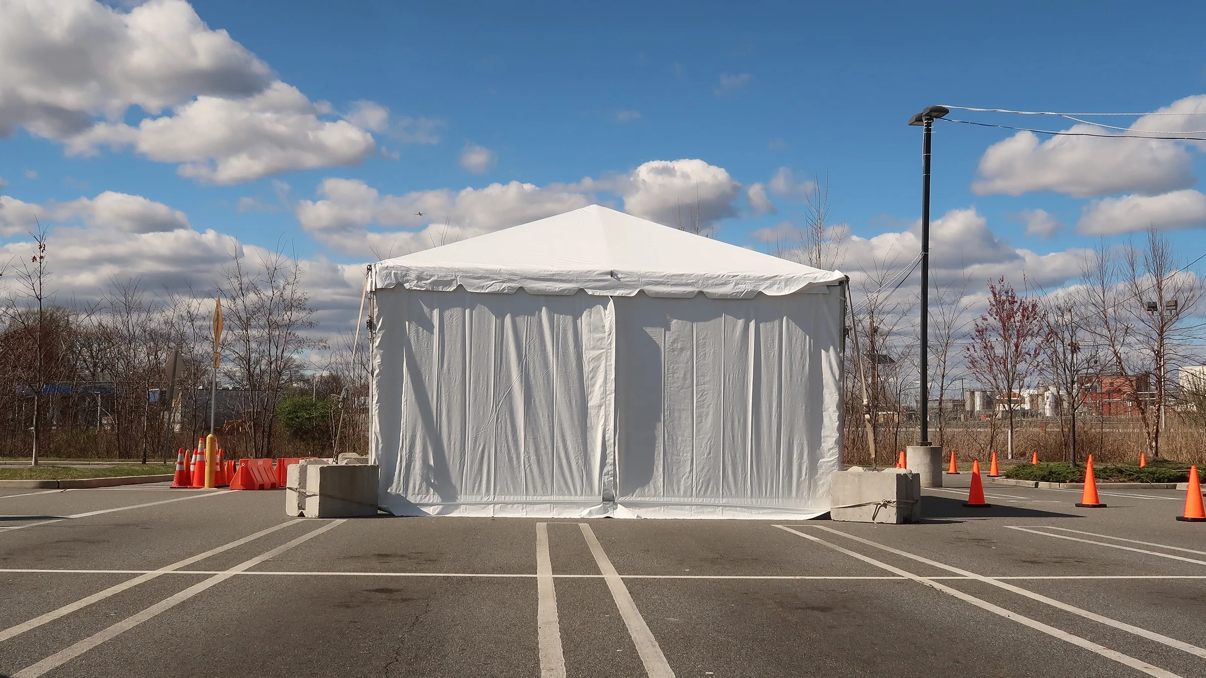 Pop-up white tent in a parking lot for a COVID-19 testing site. The parking lot is empty except for the tent and orange cones.
