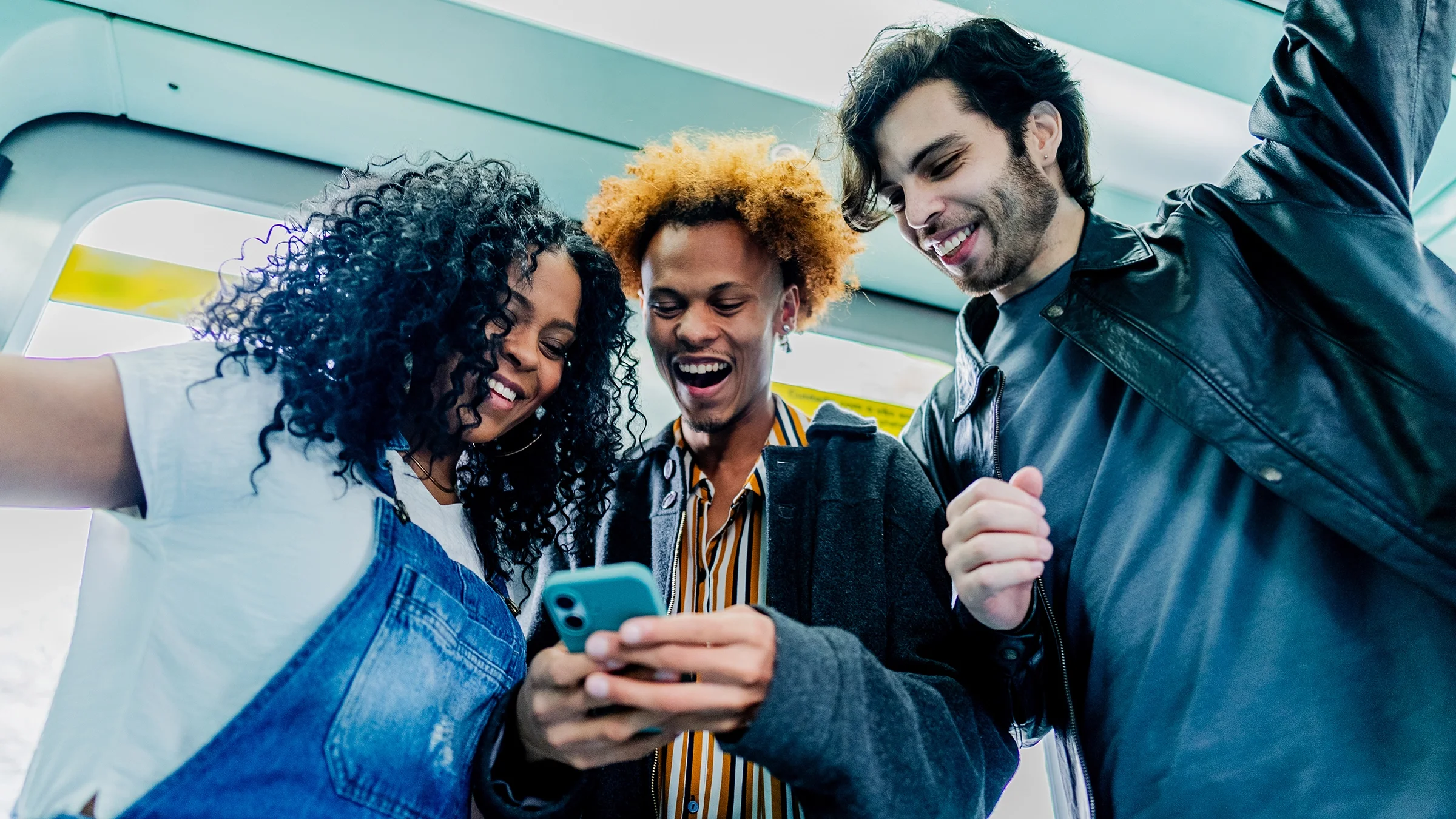 Friends look at a mobile phone while riding a train.