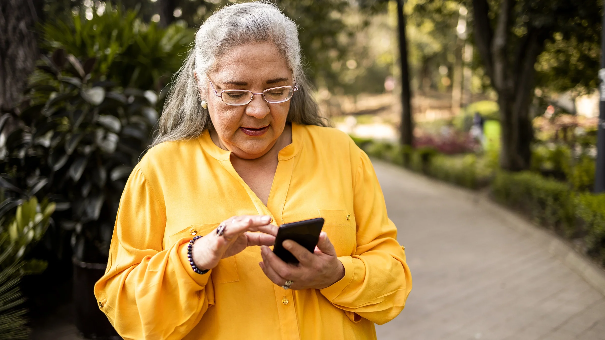 Older woman on her smart phone as she’s walking outside.