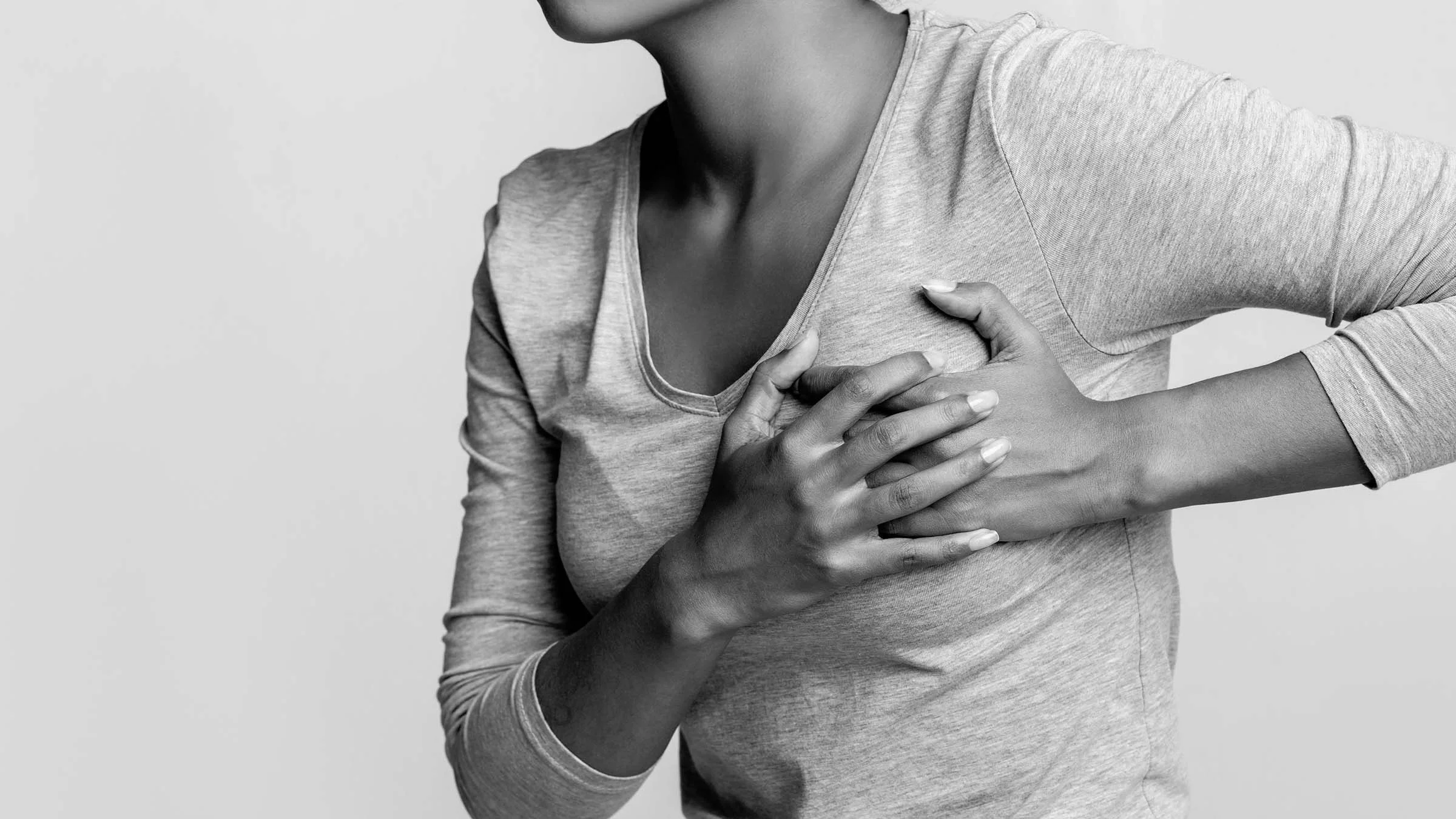 Black and white cropped shot of a woman clutching her breast in pain on a white background.