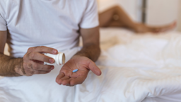A cropped shot of someone taking viagra in bed. Their partner's legs are in the blurred background.
stefanamer/iStock via Getty Images 