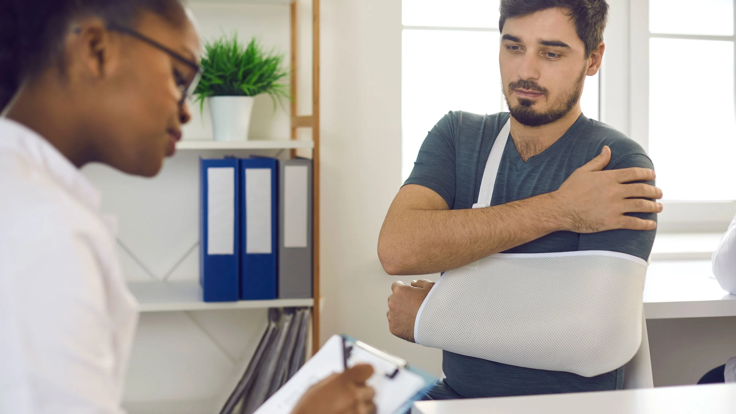 An adult has his arm in a sling in a provider’s office.