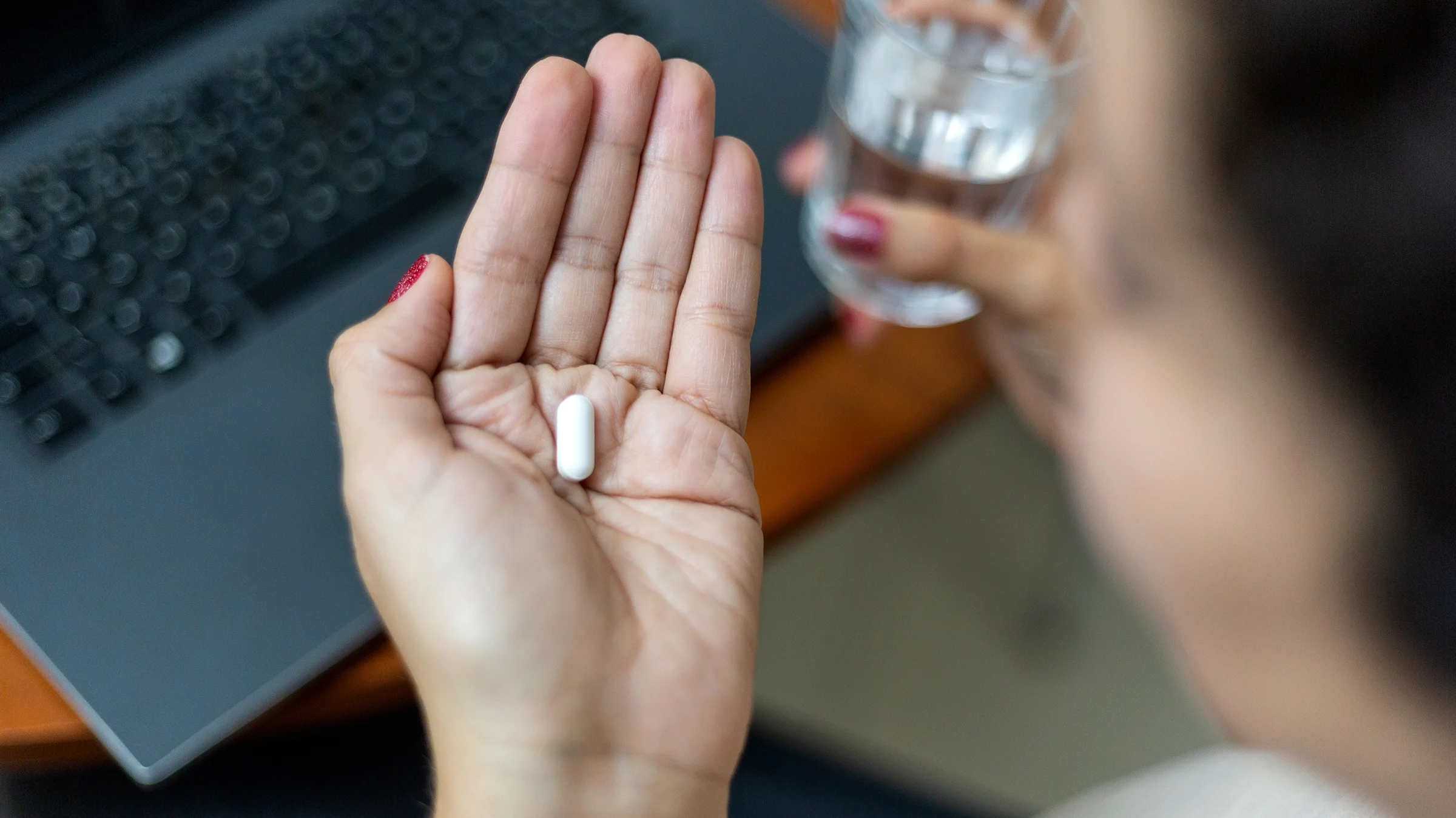 A person prepares to take a pill while holding a glass of water.