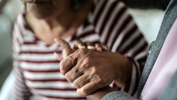 An older adult and a caregiver are holding hands.