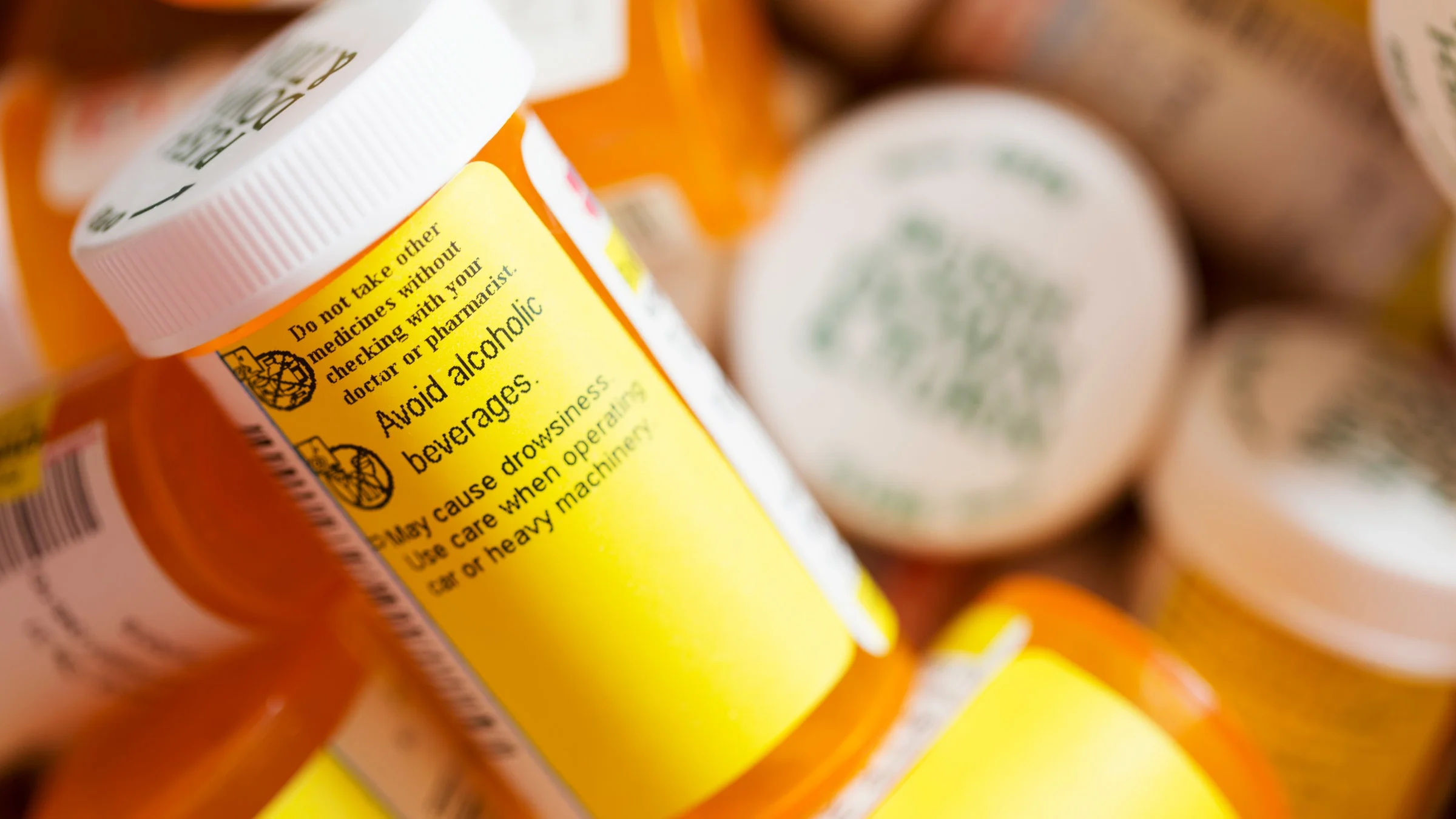 A stack of pill bottles, focused on one that says "Avoid alcoholic beverages."