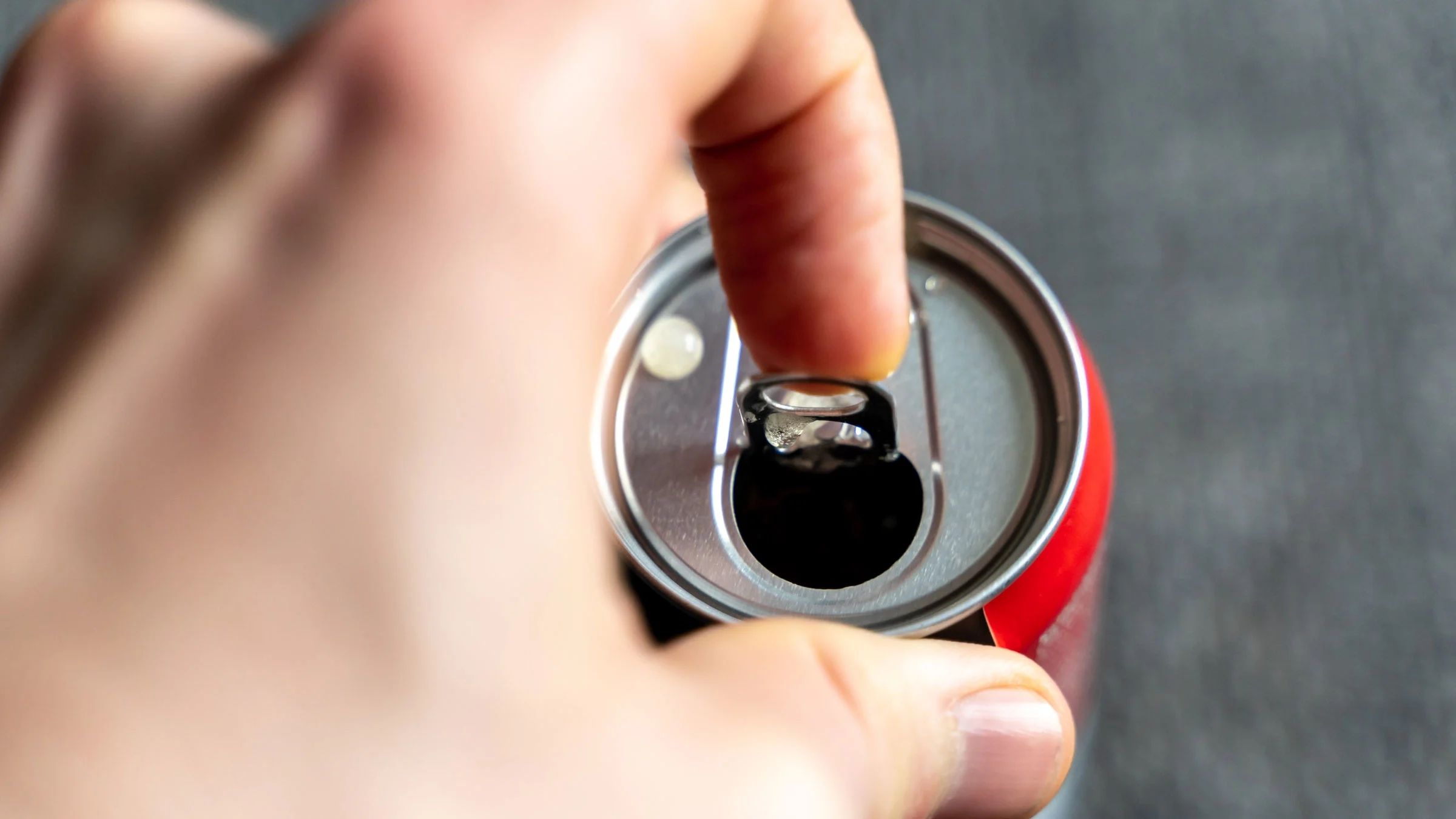 A close-up hand is opening an energy drink.