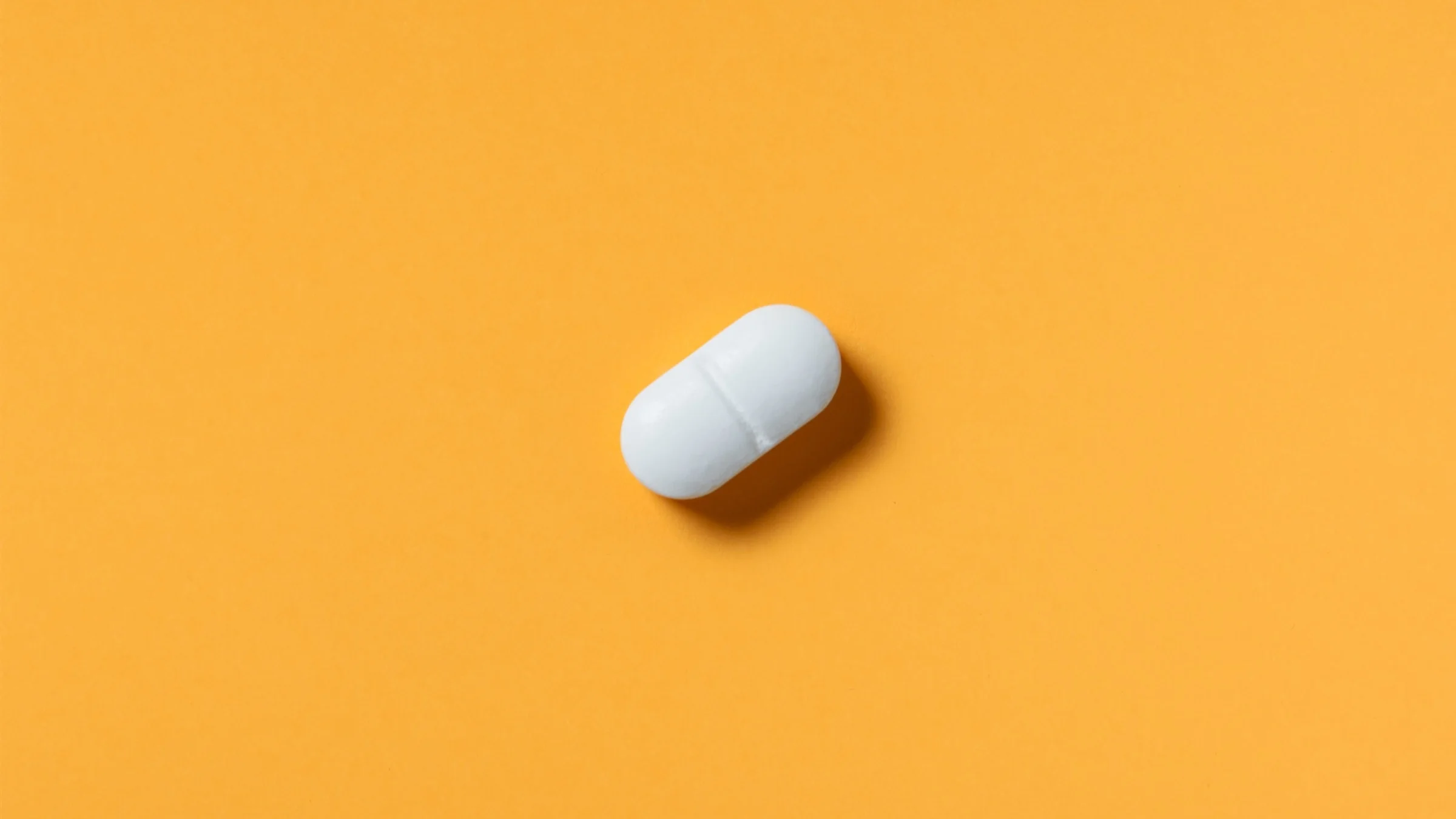 Single white oblong pill on an orange background.