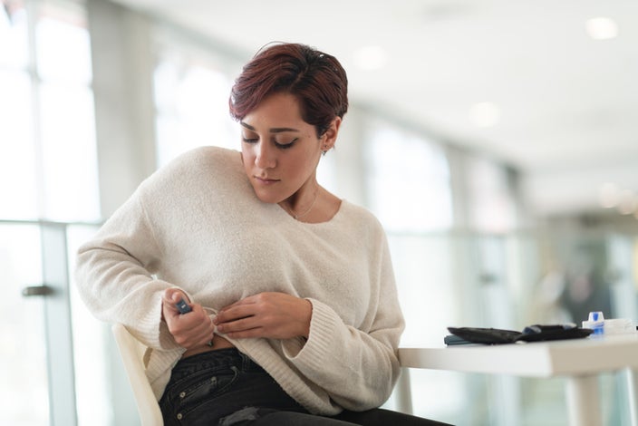 Woman sitting at a table injecting her abdomen with an insulin pen.