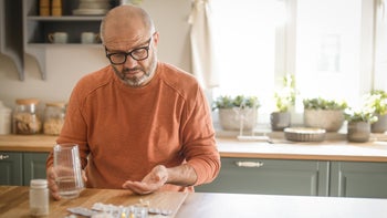 Medication: Men: older man gray beard taking pills in kitchen-1354041143