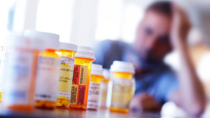 Prescription bottles sit on a table with a man in the background.Rx bottles laid out on a table with man in the background.