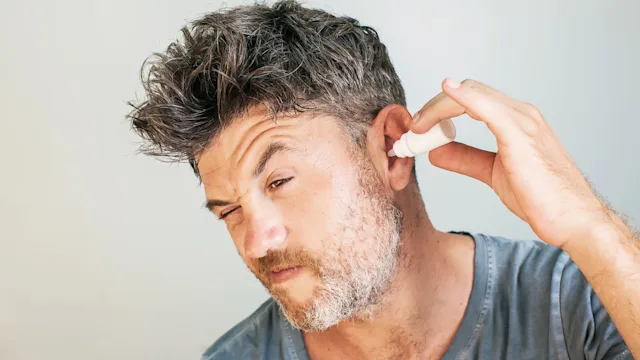 Ear infection: man using ear drops 957140496