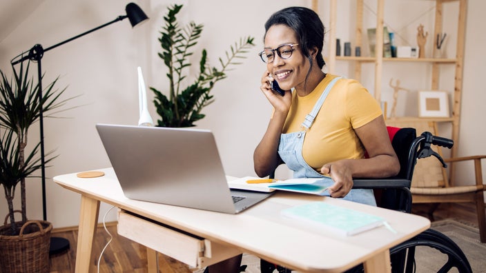 A wheelchair user at their desk, talking on the phone and taking notes.