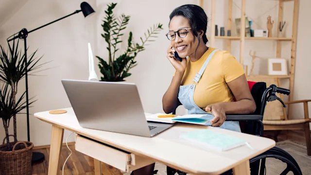 Low cost free healthcare: wheelchair user at desk on phone taking notes 1338010278