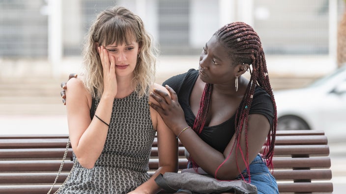 A person comforting their friend on a bench.