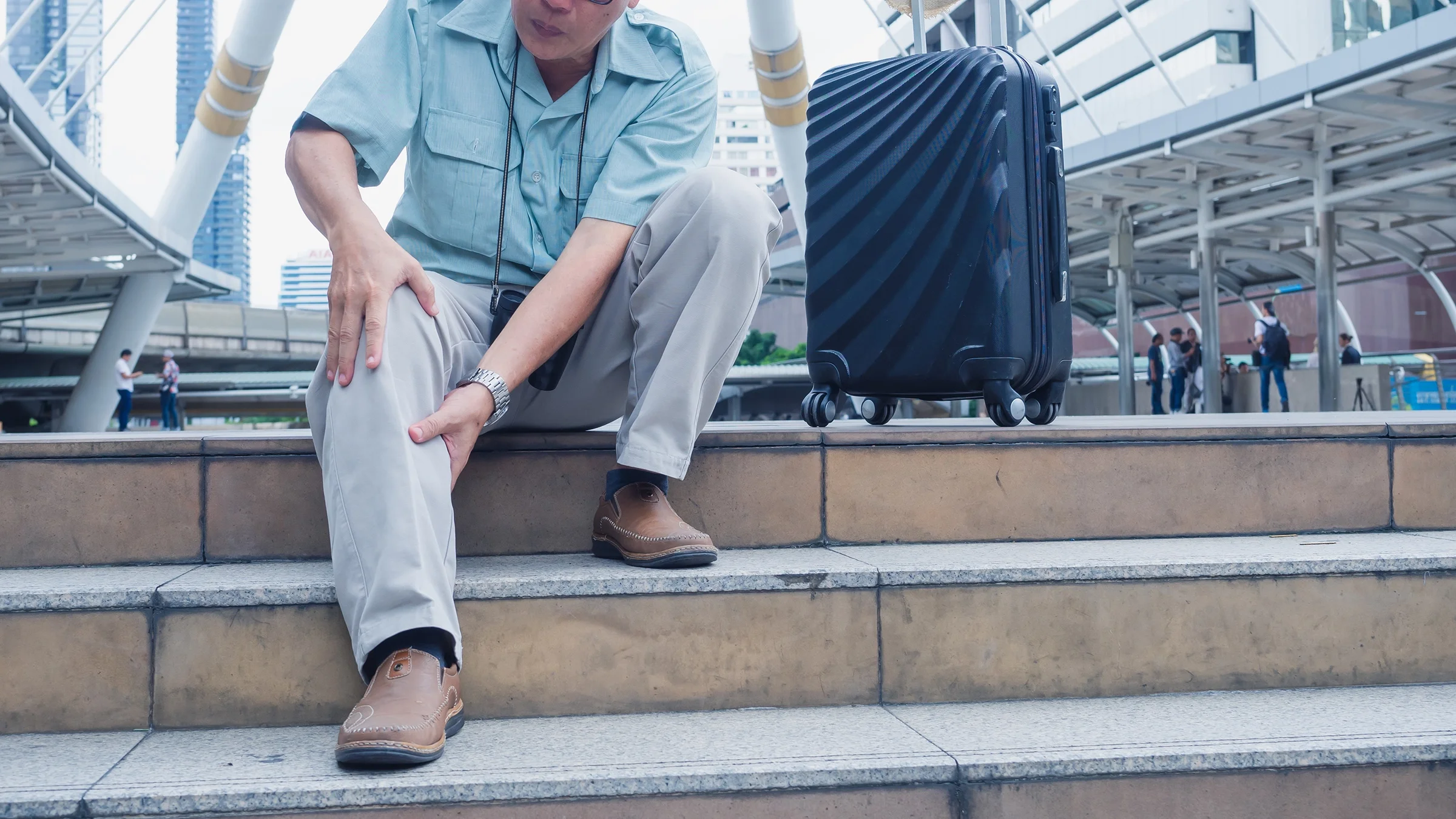 Cropped shot of a senior man stopping to rub his sore leg while traveling.
