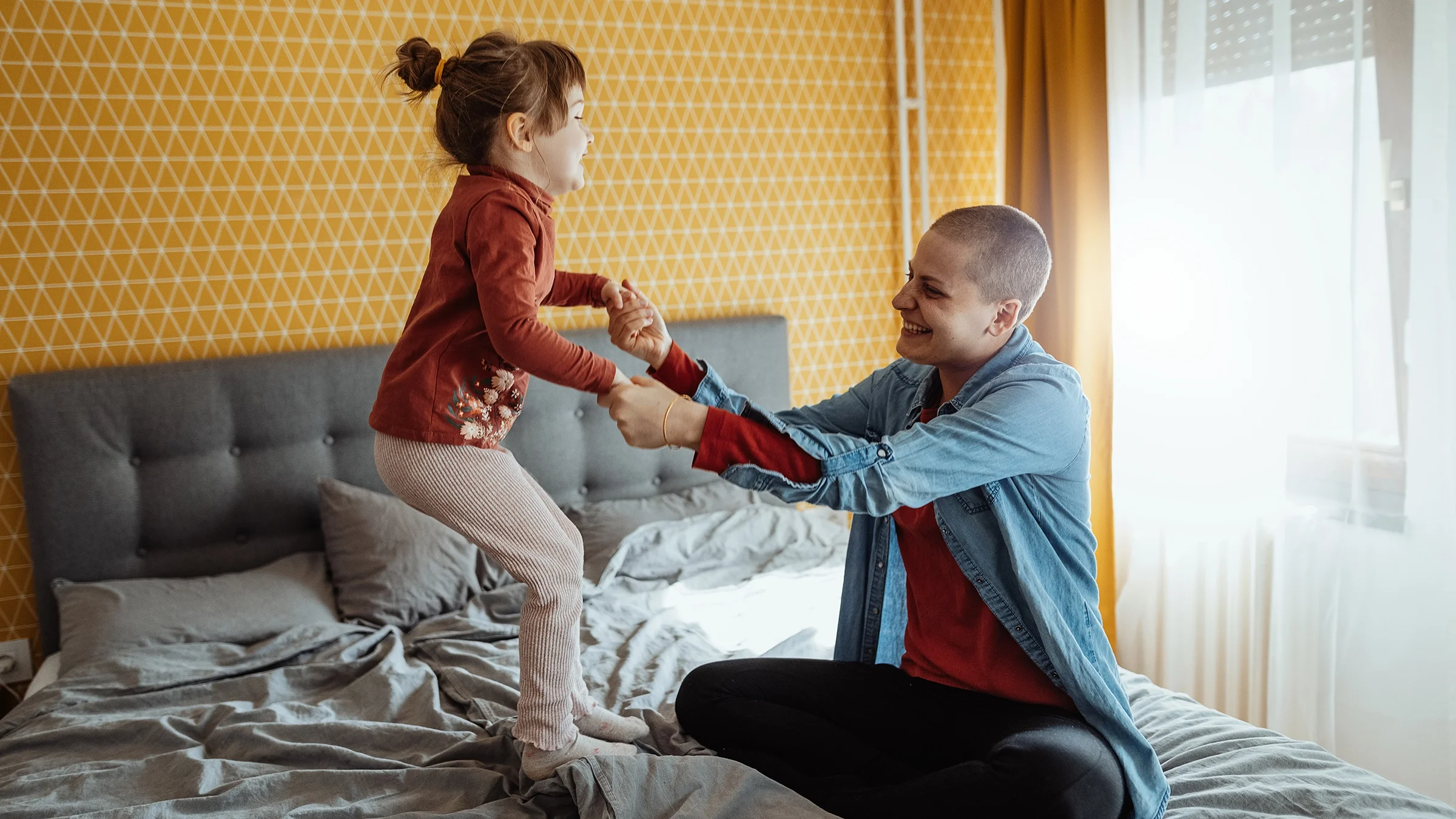 Mother playing with daughter jumping on the bed at home.