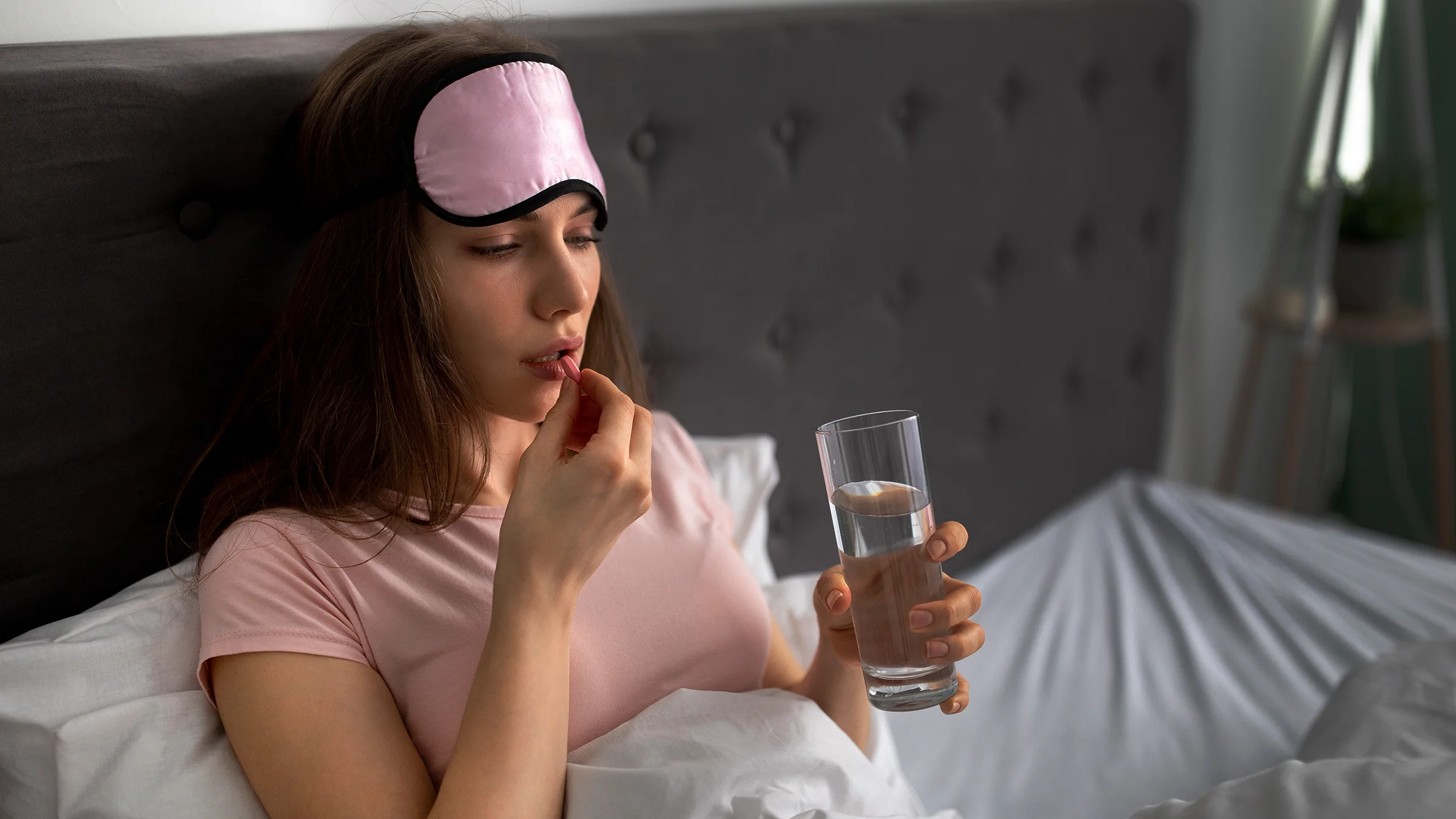A woman holding a glass of water prepares to take a pill before bed time.