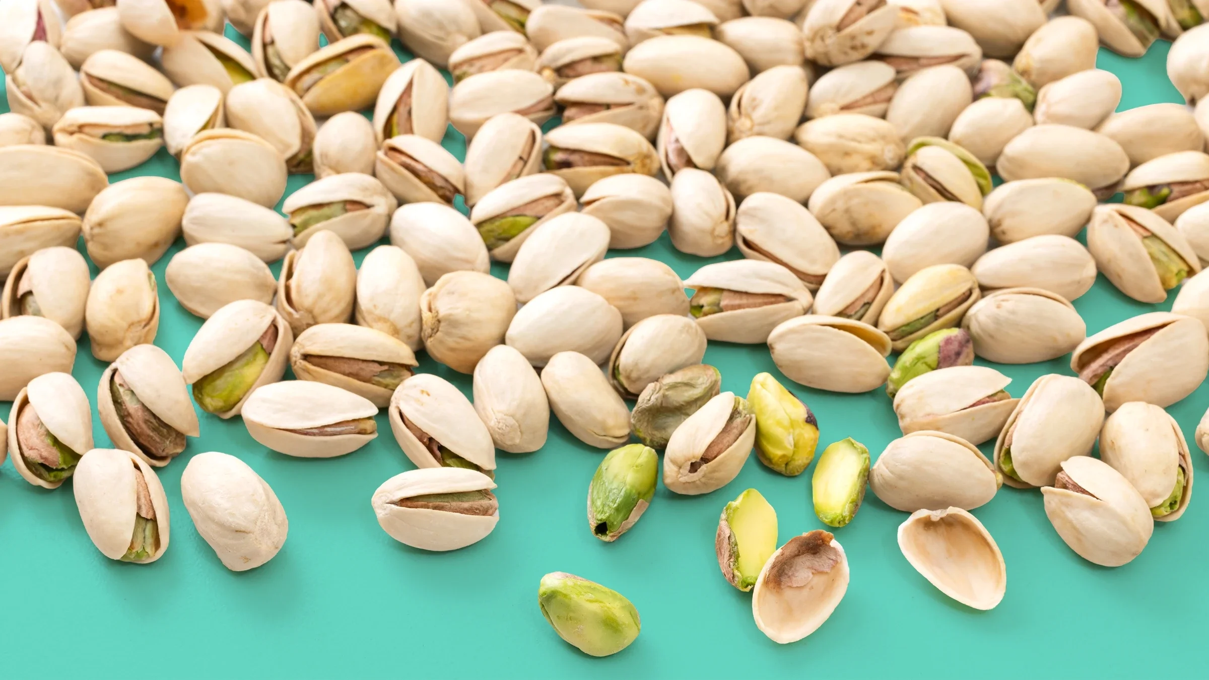Pistachio nuts with shells and kernels are scattered against a teal background.