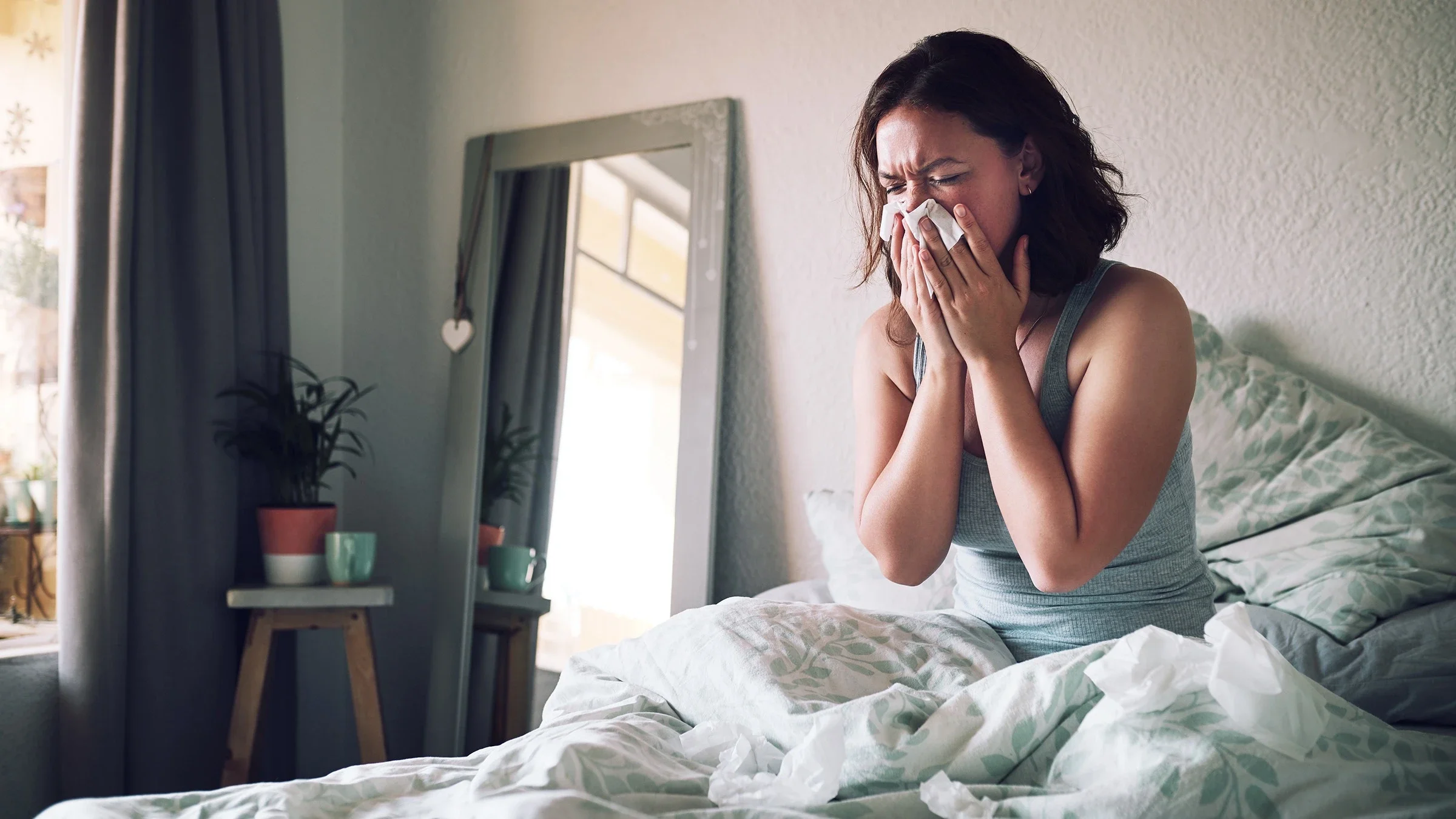 Woman sitting up in bed blowing her nose.