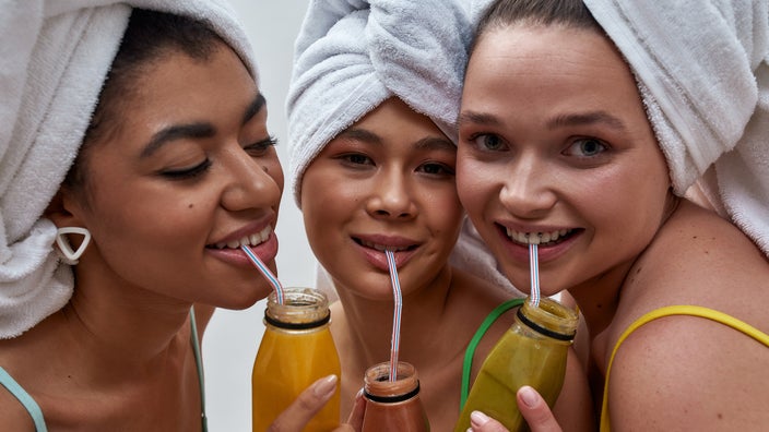 Close-up of three young friends with their hair tied up in towels and drinking detox juices together.