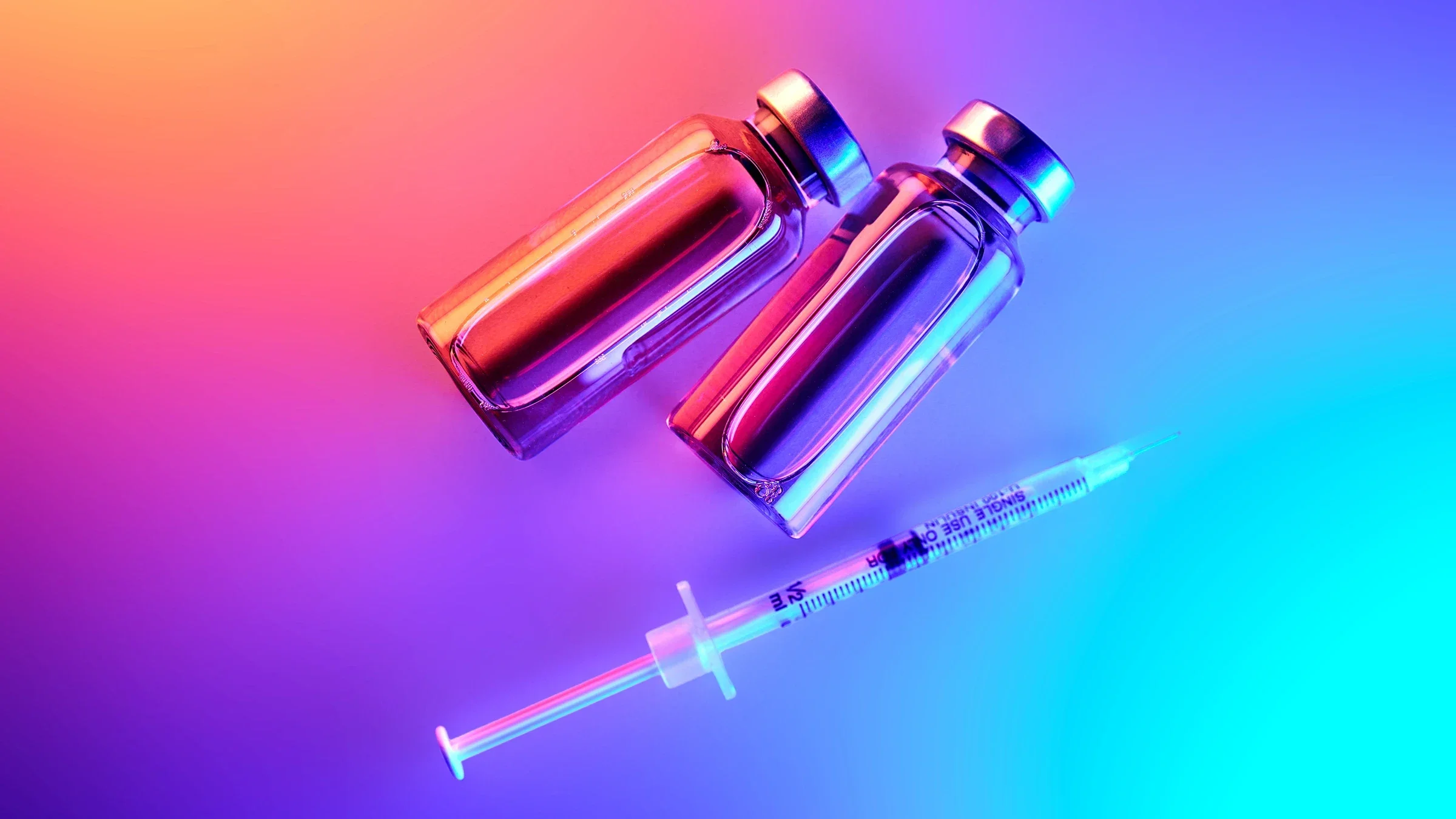 The image depicts vials and a syringe arranged on a gradient background with vibrant lighting.
Mariya Borisova/iStock via Getty Images Plus