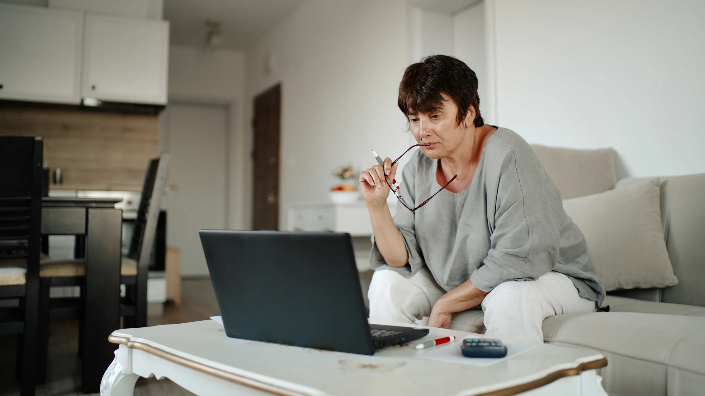 A person doing their finances on their laptop, holding their glasses.
