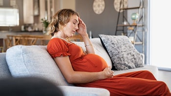 depressed pregnant woman sitting on couch-1219125246