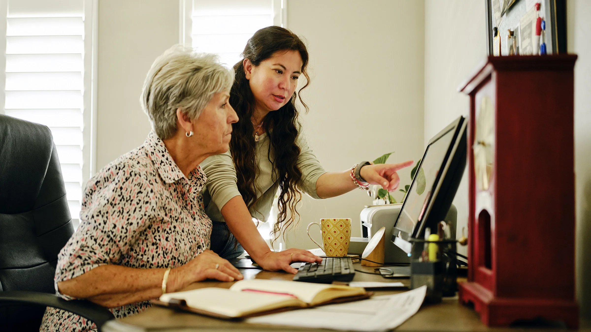 A daughter helps her mother with documents on a computer.