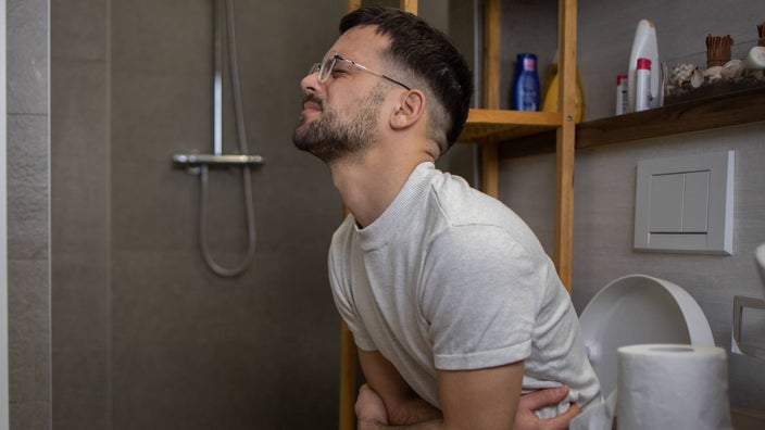 A person experiencing abdominal pain while sitting on a toilet.