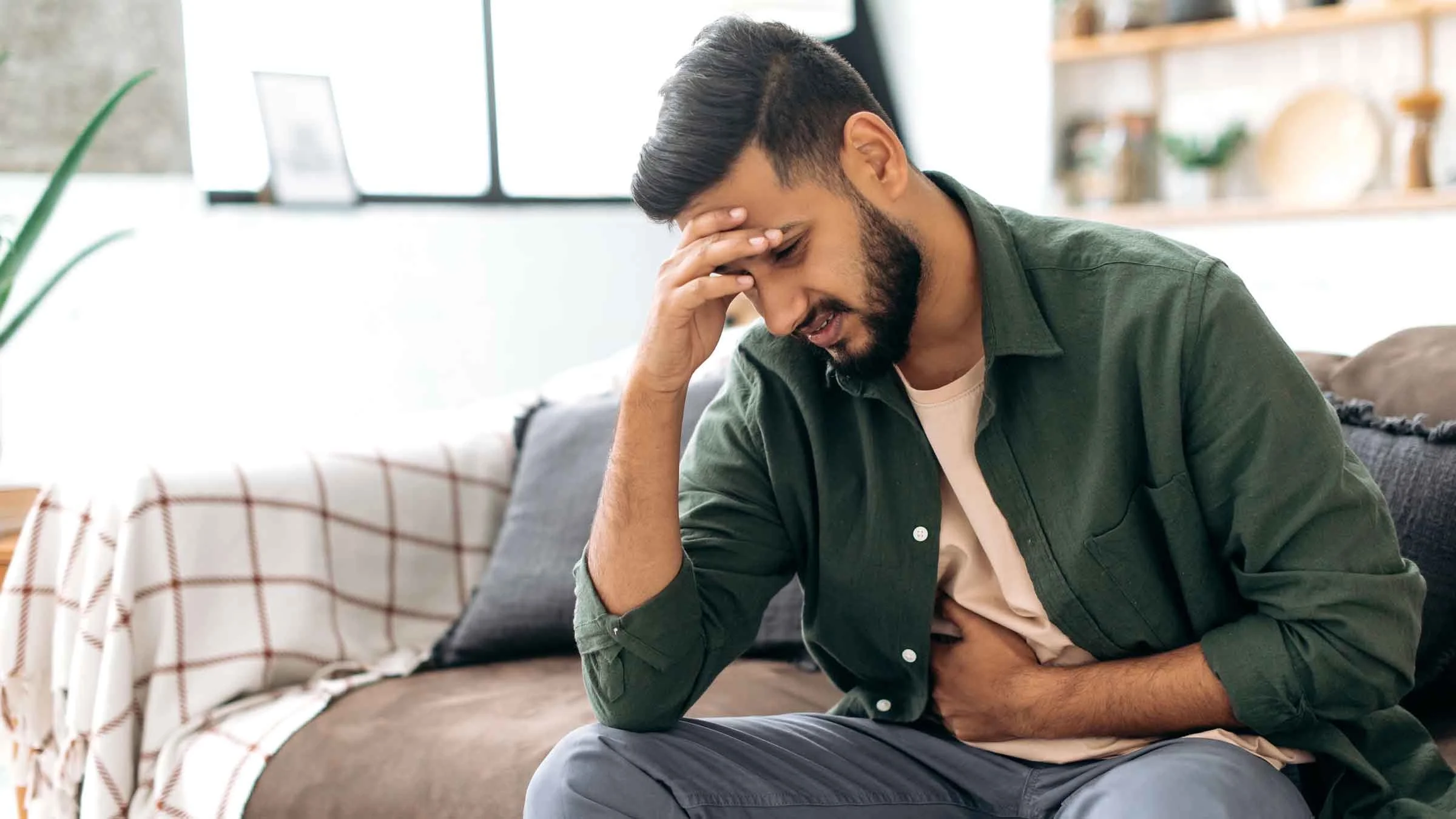 Man sits on sofa and grimaces from stomach pain