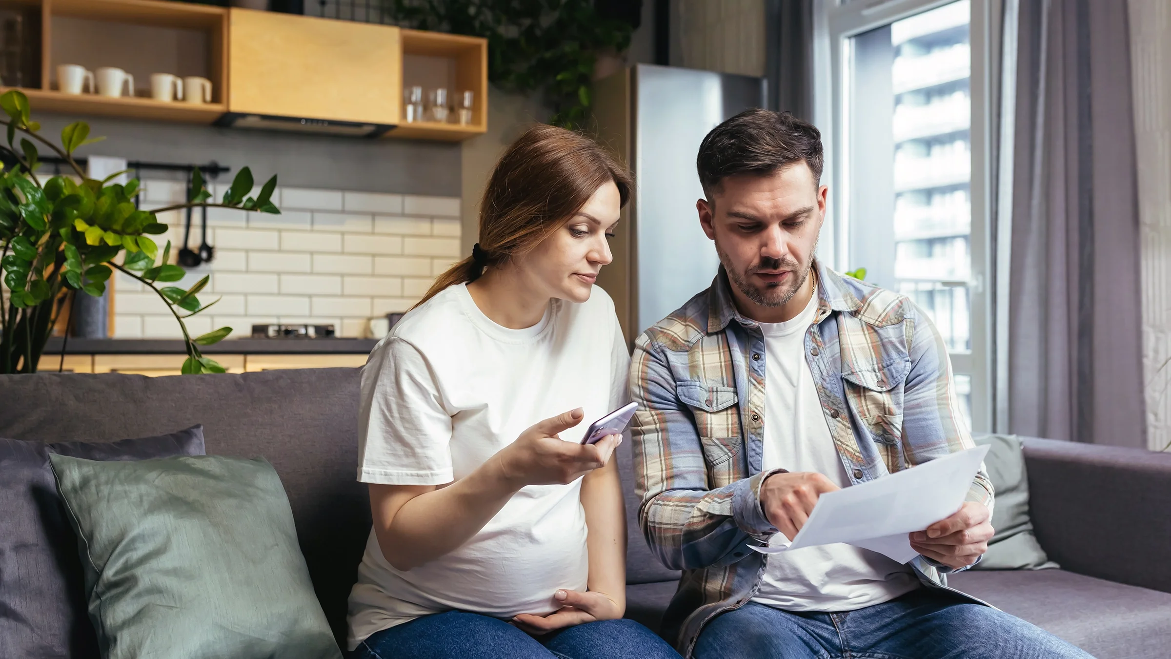 A couple reads a letter together while sitting on a sofa.