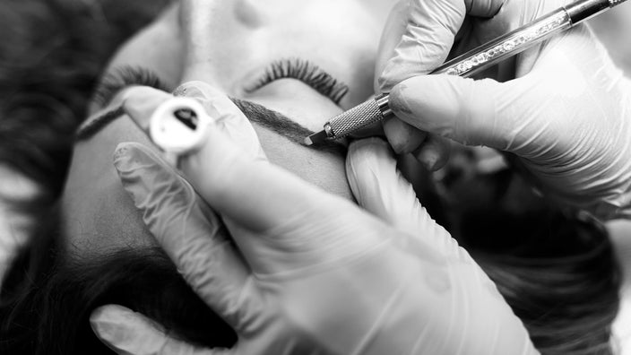 Black and white image of an adult getting an eyebrow microblading procedure.