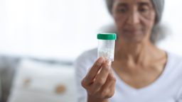 Woman holding up a bottle of white pills with a green cap. She is in the background blurry.
Wavebreakmedia/iStock via Getty Images