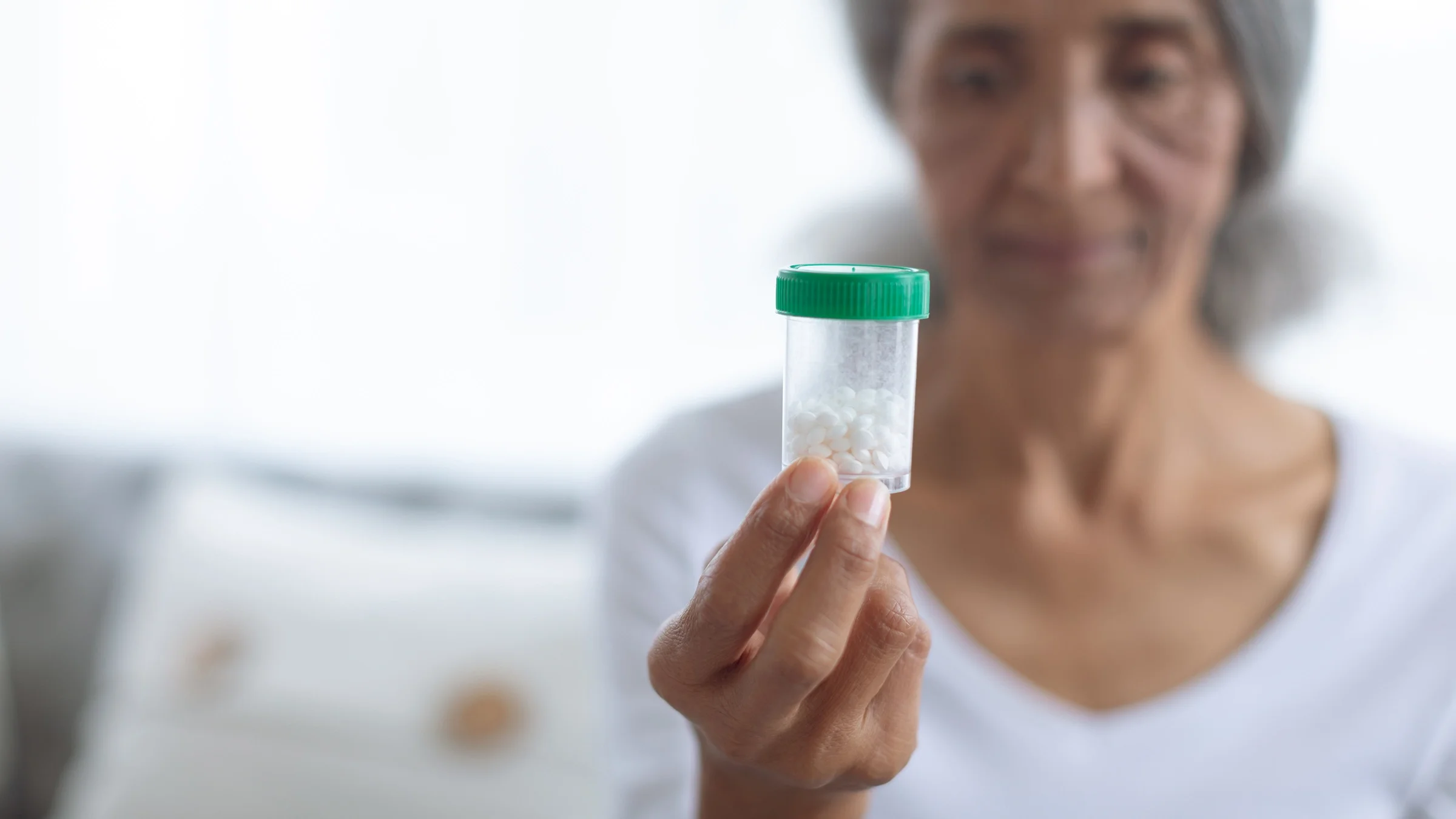 Woman holding up a bottle of white pills with a green cap. She is in the background blurry.