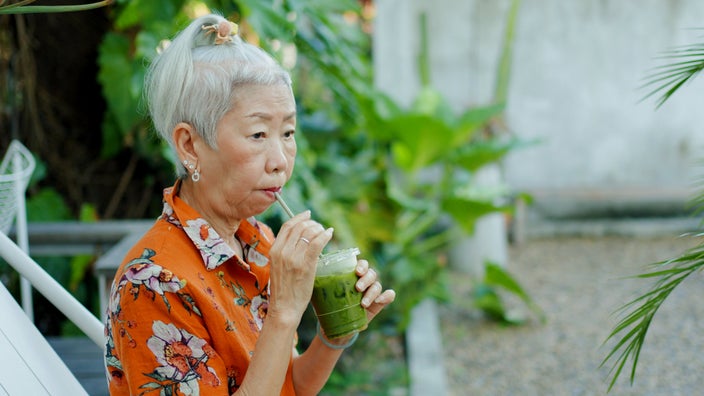 A person drinking an iced green tea with a straw.
